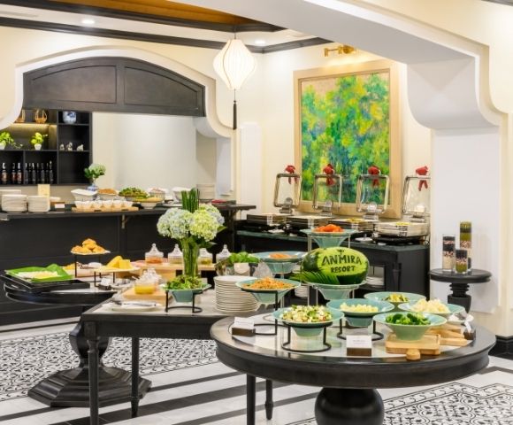 Buffet setup in a stylish dining area with tables of salads, dishes, bread, and a colorful painting on the wall.