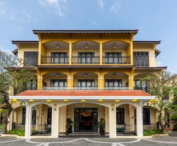 A three-story building with yellow and white facade and curved arches, set under a clear blue sky. The structure conveys a welcoming, elegant atmosphere.