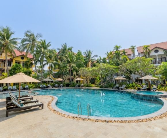 Tropical resort pool surrounded by palm trees and lounge chairs with umbrellas. Bright and sunny, conveying a relaxed and inviting atmosphere.