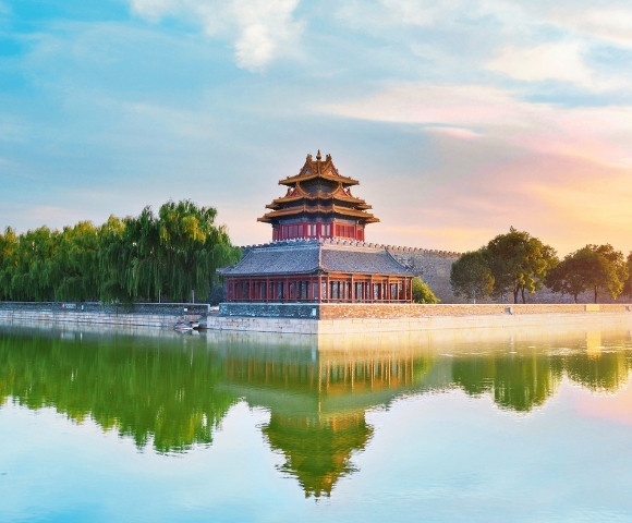 Ancient Chinese pavilion by a calm river, surrounded by lush greenery under a vibrant sunset sky, reflecting tranquility and beauty.