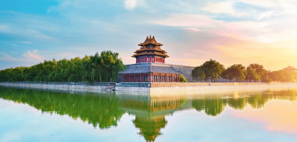 Ancient Chinese pavilion by a calm river, surrounded by lush greenery under a vibrant sunset sky, reflecting tranquility and beauty.