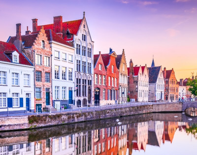 Colorful historic buildings lining a calm canal with clear reflections at sunset in a European town.