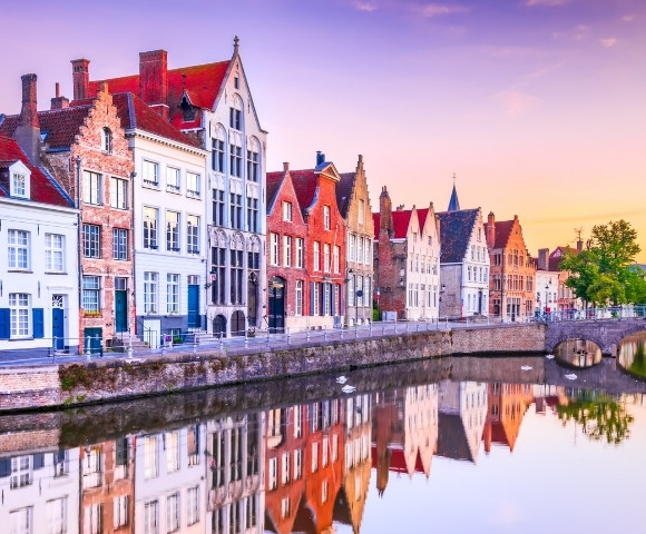 Colorful historic buildings lining a calm canal with clear reflections at sunset in a European town.