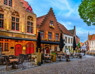 Cobblestone street with outdoor café seating, historic brick buildings with stepped gables, and vibrant evening lighting under a blue sky.