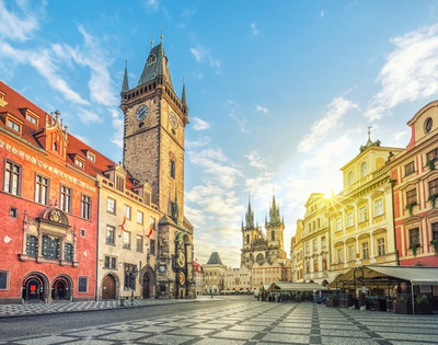 Scenic view of Prague's Old Town Square featuring historic buildings and the iconic clock tower under a bright blue sky.