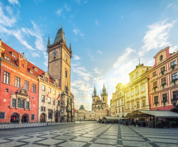 Scenic view of Prague's Old Town Square featuring historic buildings and the iconic clock tower under a bright blue sky.