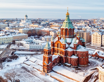 Aerial view of a snow-covered cityscape featuring a historic church with a green dome and red brick architecture in winter.