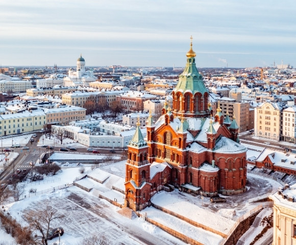 Aerial view of a snow-covered cityscape featuring a historic church with a green dome and red brick architecture in winter.