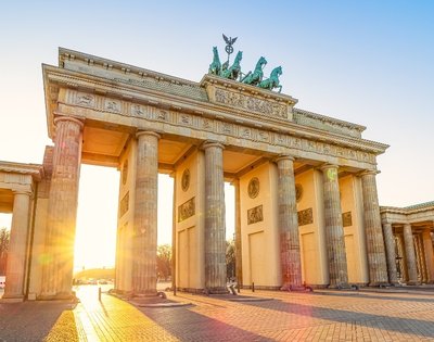 Sunset illuminates the iconic Brandenburg Gate in Berlin. The sun casts a warm glow through the columns, creating a serene and majestic atmosphere.