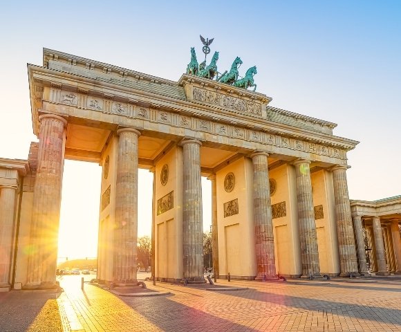Sunset illuminates the iconic Brandenburg Gate in Berlin. The sun casts a warm glow through the columns, creating a serene and majestic atmosphere.