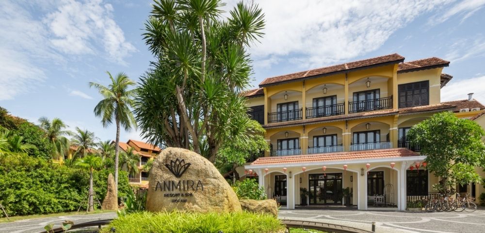 Exterior view of Anmira Resort & Spa with tropical landscaping, palm trees, and a clear sky in the background.