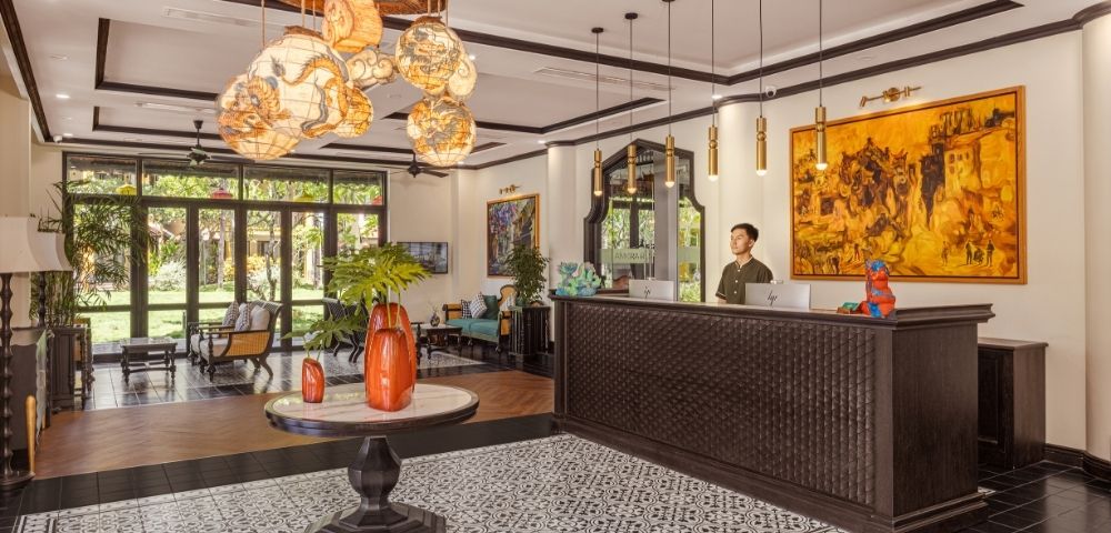 A hotel reception area with a dark wood counter, a large abstract painting, and decorative lighting.