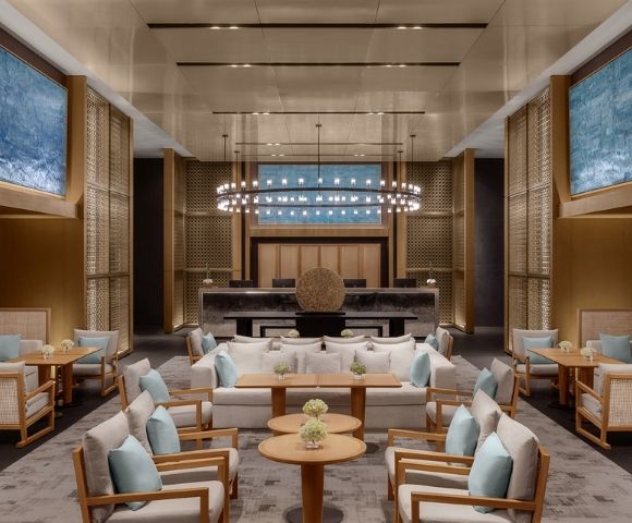 A luxurious hotel lobby with modern seating arrangements, a grand reception desk, and large abstract blue paintings on the walls.