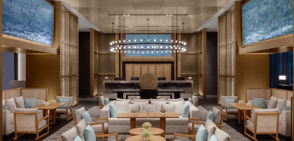 A luxurious hotel lobby with modern seating arrangements, a grand reception desk, and large abstract blue paintings on the walls.