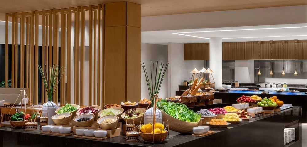Buffet table laden with various fresh fruits, salads, and breads in a well-lit dining area.