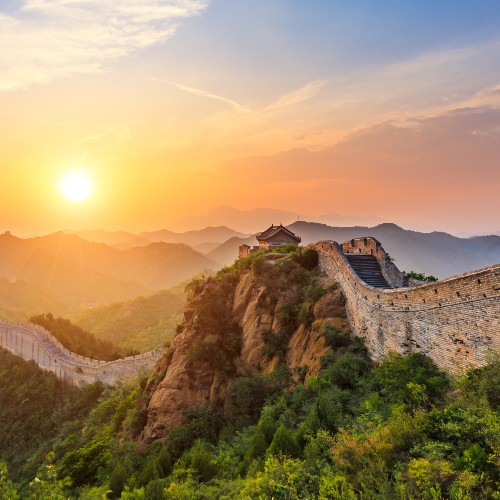 Sunset over the Great Wall of China, with lush green hills and a vibrant sky. The scene evokes a sense of majesty and tranquility.