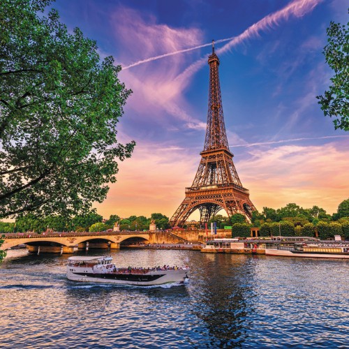 A picturesque view of the Eiffel Tower at sunset, framed by lush trees. A boat cruises the Seine River, under a sky painted with pink and orange hues.