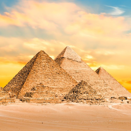 The image shows the iconic pyramids of Giza under a vibrant, golden sunset sky. The desert foreground enhances their ancient, majestic presence.