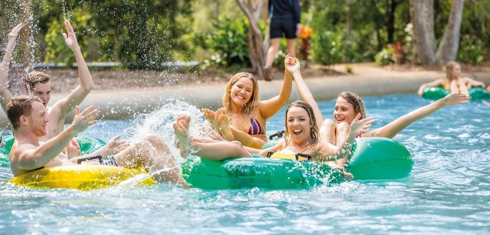 Group of friends laughing and splashing water while riding inner tubes down a lazy river.