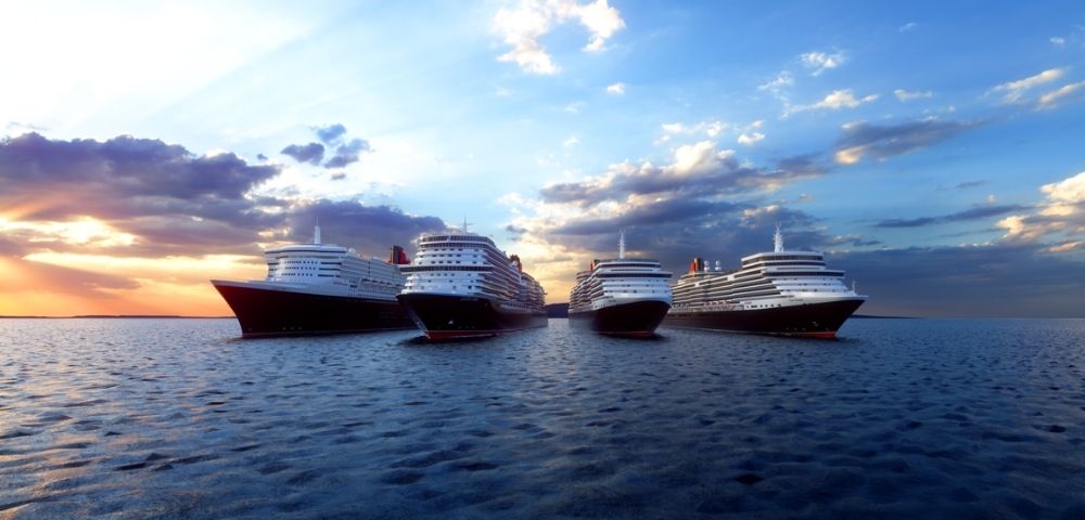 Large cruise ships aligned on calm ocean water during sunset, with golden sunlight on the left and a blue sky with scattered clouds above