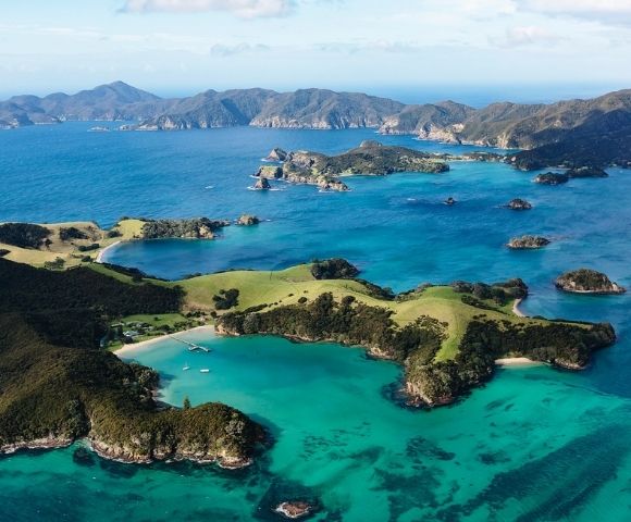 Aerial view of a vibrant turquoise bay surrounded by lush green islands and rugged hills under a partly cloudy sky.