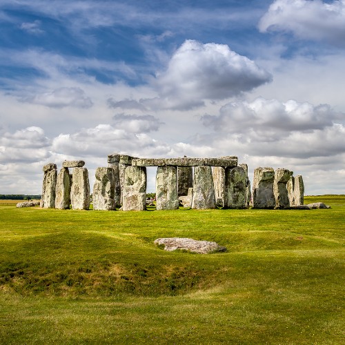Stonehenge under a partly cloudy sky, with large stone slabs standing on a lush green field, conveying a serene and ancient atmosphere.