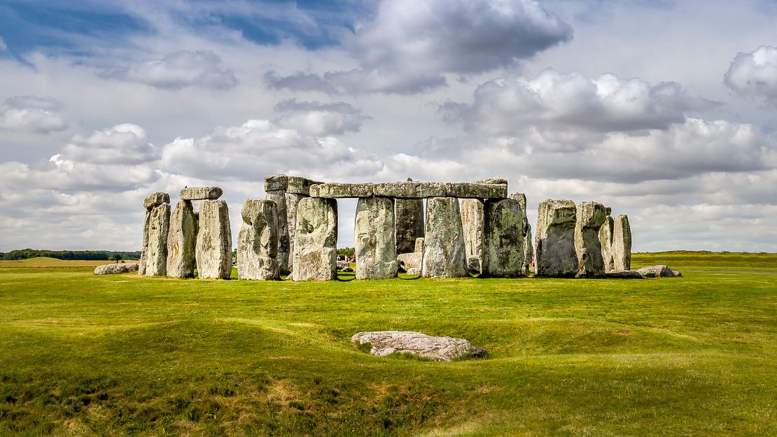 Stonehenge under a partly cloudy sky, with large stone slabs standing on a lush green field, conveying a serene and ancient atmosphere.