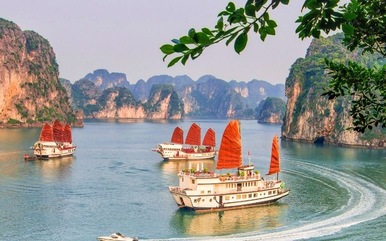 Traditional junks with orange sails navigate a serene bay surrounded by dramatic limestone karsts.