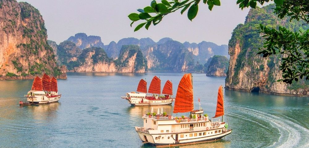 Traditional junks with orange sails navigate a serene bay surrounded by dramatic limestone karsts.