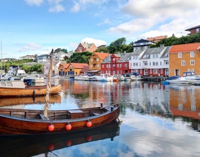 Wooden boats moored in a harbor with colorful buildings lining the waterfront under a blue sky with clouds