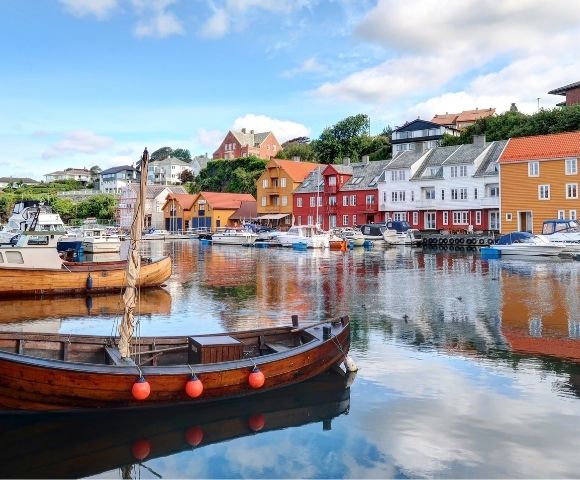 Wooden boats moored in a harbor with colorful buildings lining the waterfront under a blue sky with clouds