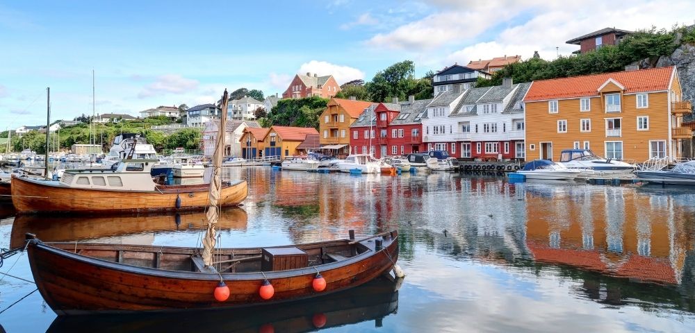 Wooden boats moored in a harbor with colorful buildings lining the waterfront under a blue sky with clouds