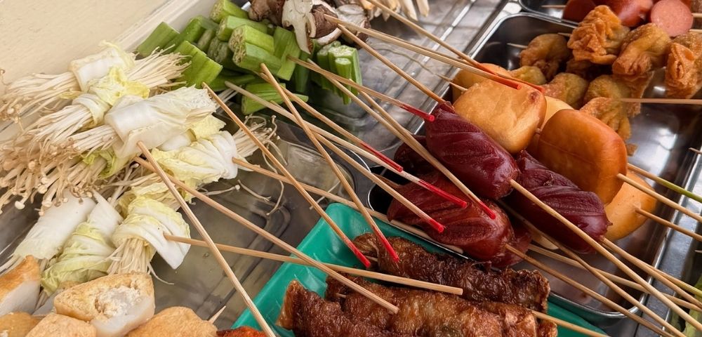 Assortment of skewered food items including enoki mushrooms wrapped in napa cabbage, sausages, and fried dough.