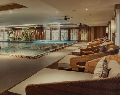 An indoor spa area featuring a serene pool, comfortable lounge chairs, and decorative lighting.
