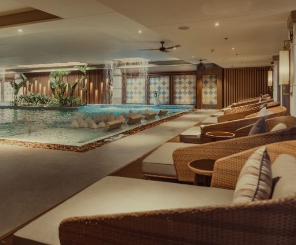 An indoor spa area featuring a serene pool, comfortable lounge chairs, and decorative lighting.
