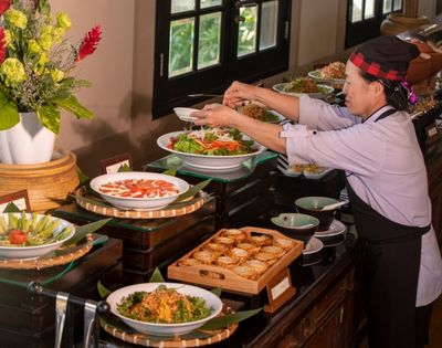 A chef arranging a colorful buffet spread with fresh salads and various dishes in a beautifully decorated dining area.