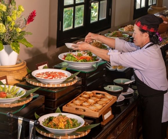 A chef arranging a colorful buffet spread with fresh salads and various dishes in a beautifully decorated dining area.