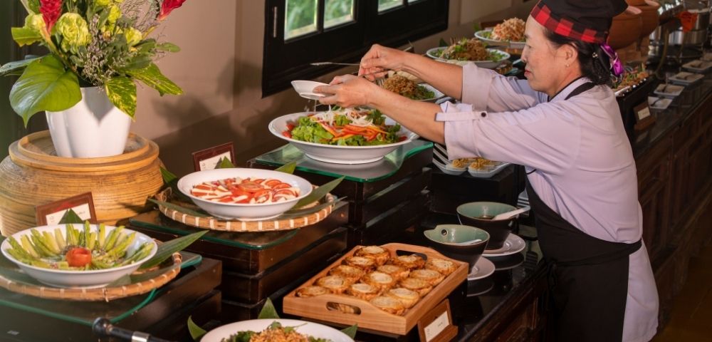 A chef arranging a colorful buffet spread with fresh salads and various dishes in a beautifully decorated dining area.