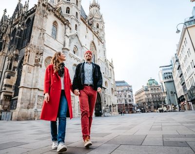 A couple strolls in a city square, with a historic cathedral in the background. They are smiling, exuding a sense of joy and exploration.