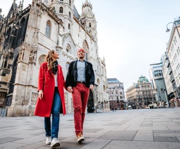 A couple strolls in a city square, with a historic cathedral in the background. They are smiling, exuding a sense of joy and exploration.