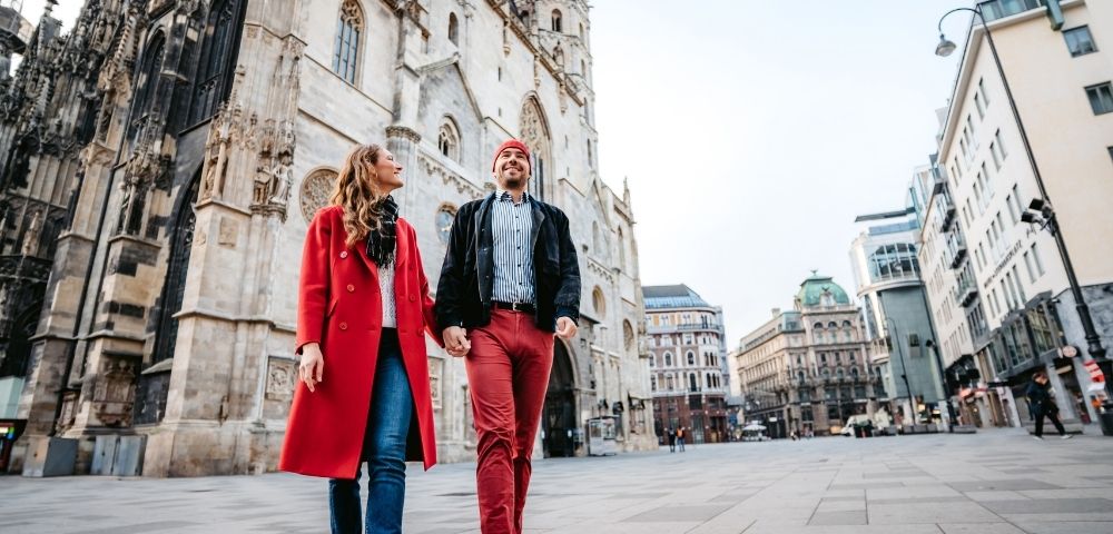 A couple strolls in a city square, with a historic cathedral in the background. They are smiling, exuding a sense of joy and exploration.