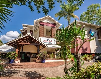 The Freestyle Resort entrance with a covered walkway and tropical plants under a bright blue sky with scattered clouds.