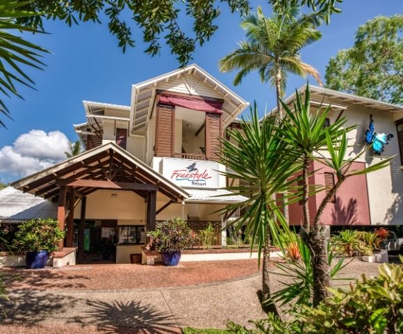 The Freestyle Resort entrance with a covered walkway and tropical plants under a bright blue sky with scattered clouds.