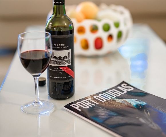 A glass of red wine sits next to a bottle of Wynn's Coonawarra Estate Cabernet Shiraz Merlot 2015 and a magazine titled 
