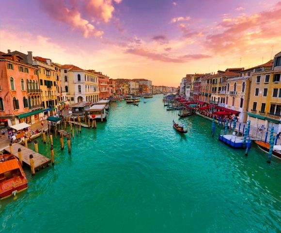 A picturesque canal in Venice at sunset, with vibrant turquoise water, lined with colorful historic buildings and gondolas.