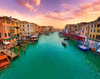 A picturesque canal in Venice at sunset, with vibrant turquoise water, lined with colorful historic buildings and gondolas.