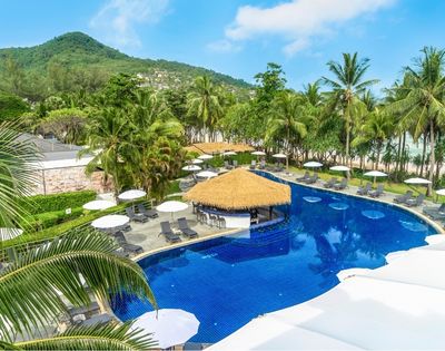 Resort pool surrounded by lounge chairs and umbrellas, with palm trees and a green mountain in the background under a clear blue sky.