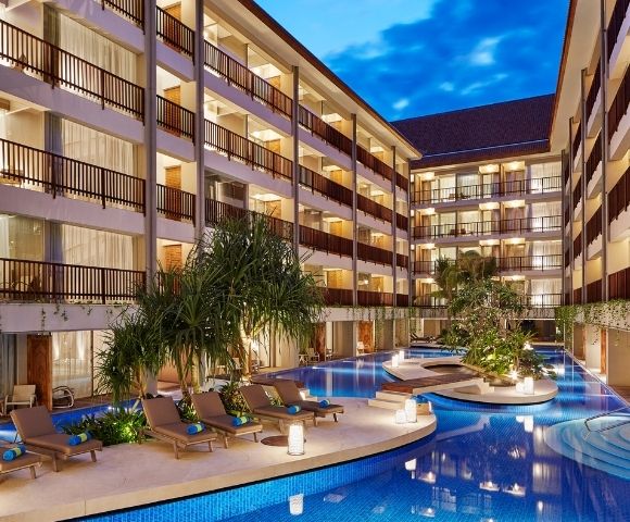 A courtyard hotel with balconies overlooking a blue swimming pool and lounge chairs.