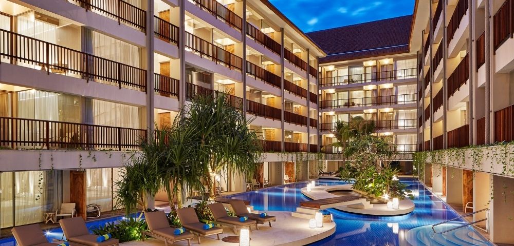A courtyard hotel with balconies overlooking a blue swimming pool and lounge chairs.