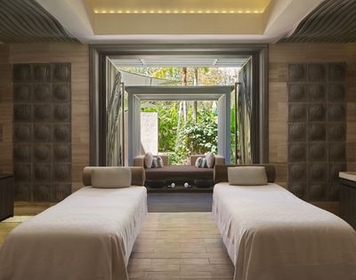 Two massage tables with light-colored linens in a spa room, with open doors revealing a lush garden view.
